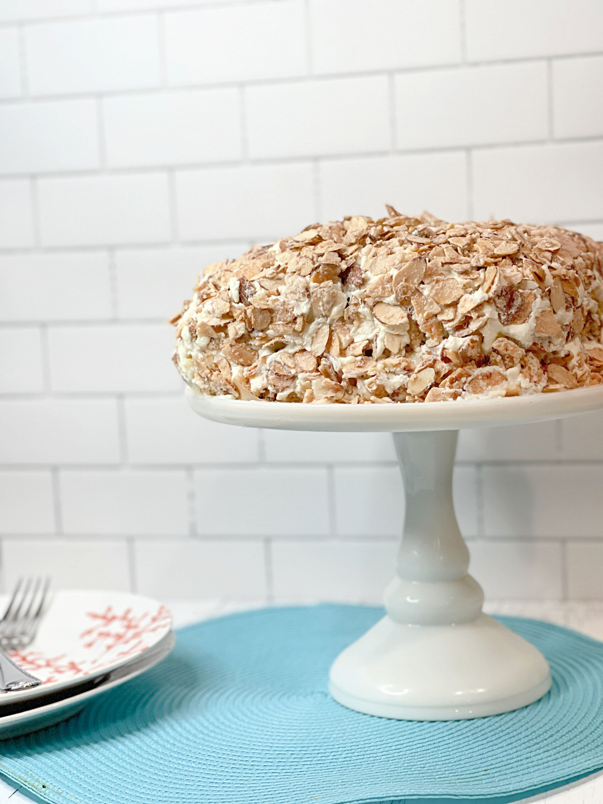 Side view of a Burnt Almond Torte cake on a white cake plate sitting on a blue placemat.