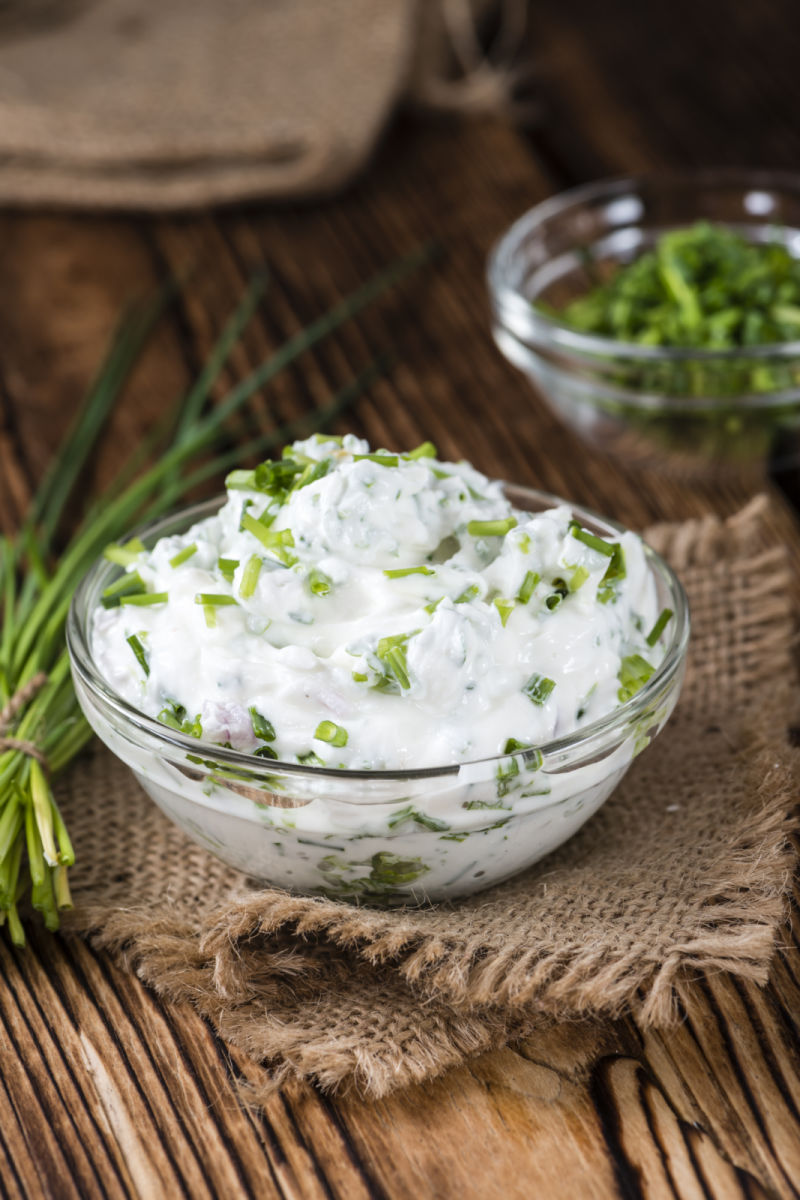 Glass bowl of herbed cream cheese with a bowl of minced chives on the side.