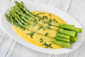White serving dish with Windows On The World Asparagus In Chive Hollandaise Sauce and sitting on a white wooden surface.