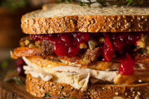 BLACK FRIDAY SANDWICH ON A WOODEN BOARD - LEFTOVER THANKSGIVING TURKEY, DRESSING, GRAVY, AND CRANBERRY SAUCE ON WHOLE WHEAT BREAD.