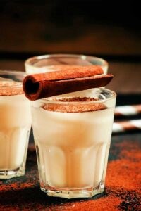 Black tray with three glasses of Healthy Eggnog Smoothies garnished with ground cinnamon, nutmeg, and a cinnamon stick.