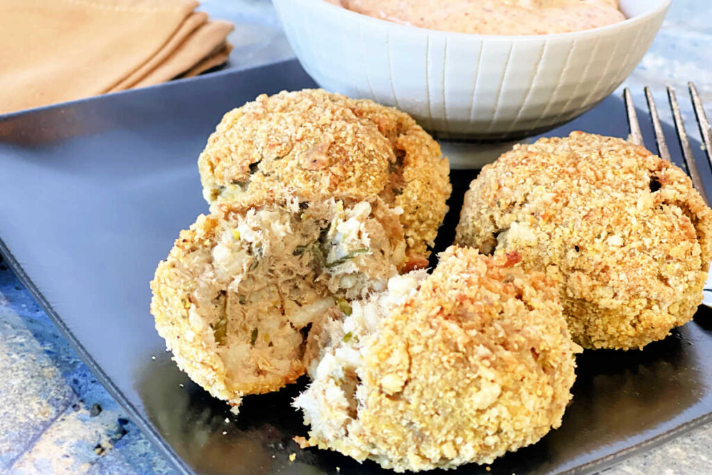 Brown plate with two whole and one split baked Cajun boudin balls with remoulade sauce.