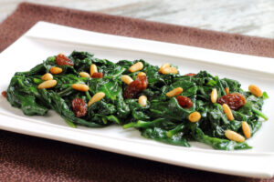 White platter with Catalan Spinach - sauteed spinach with raisins, pine nuts, and sherry vinegar.