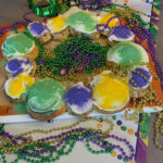 Kid-Friendly King Cake decorated with Mardi Gras beads, coins, and masks and placed on a Mardi Gras table runner.