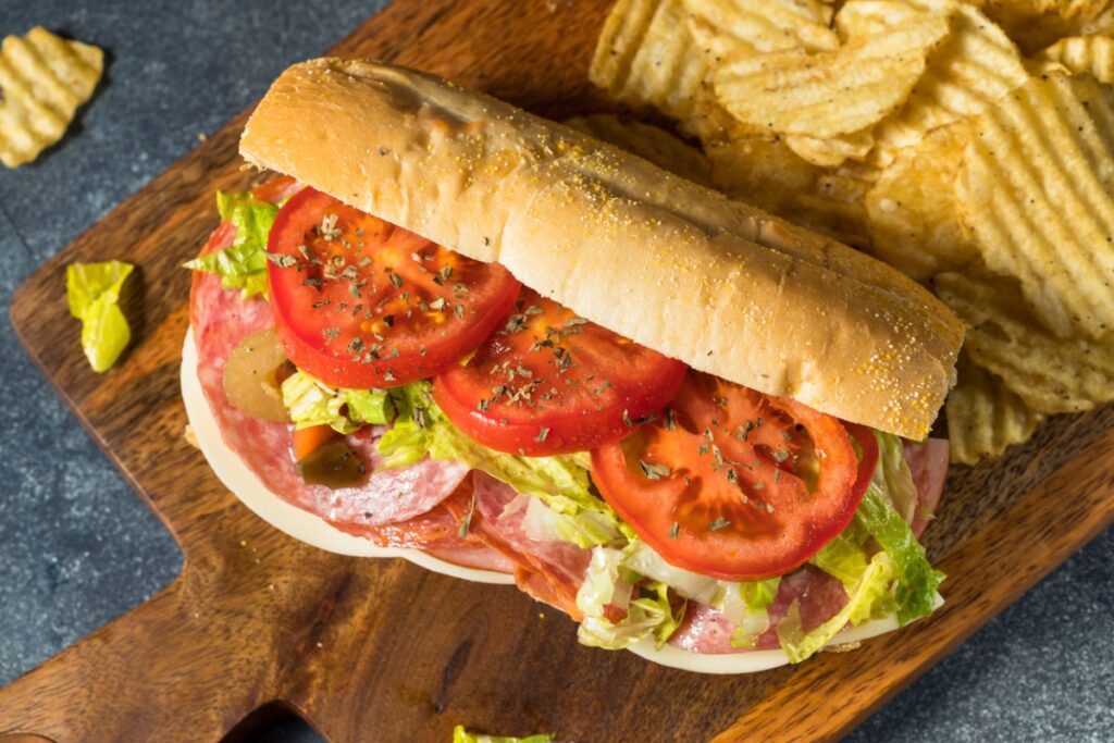 Wooden board with a Philly-Style Italian Hoagie and chips on the side.