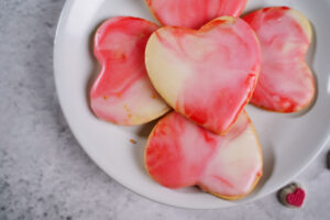 Gray marble background with a white plate with heart shaped Valentine sugar cookies with red, pink, and white marble icing.