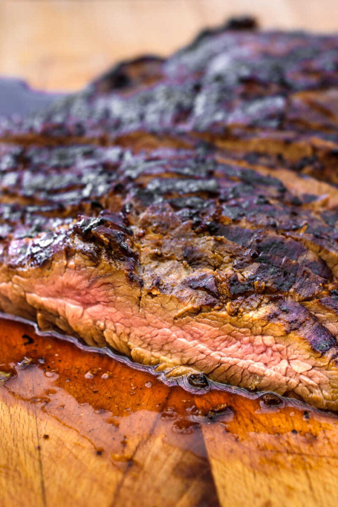 Close up of grilled citrus marinated flank steak, sliced, on a wooden cutting board.