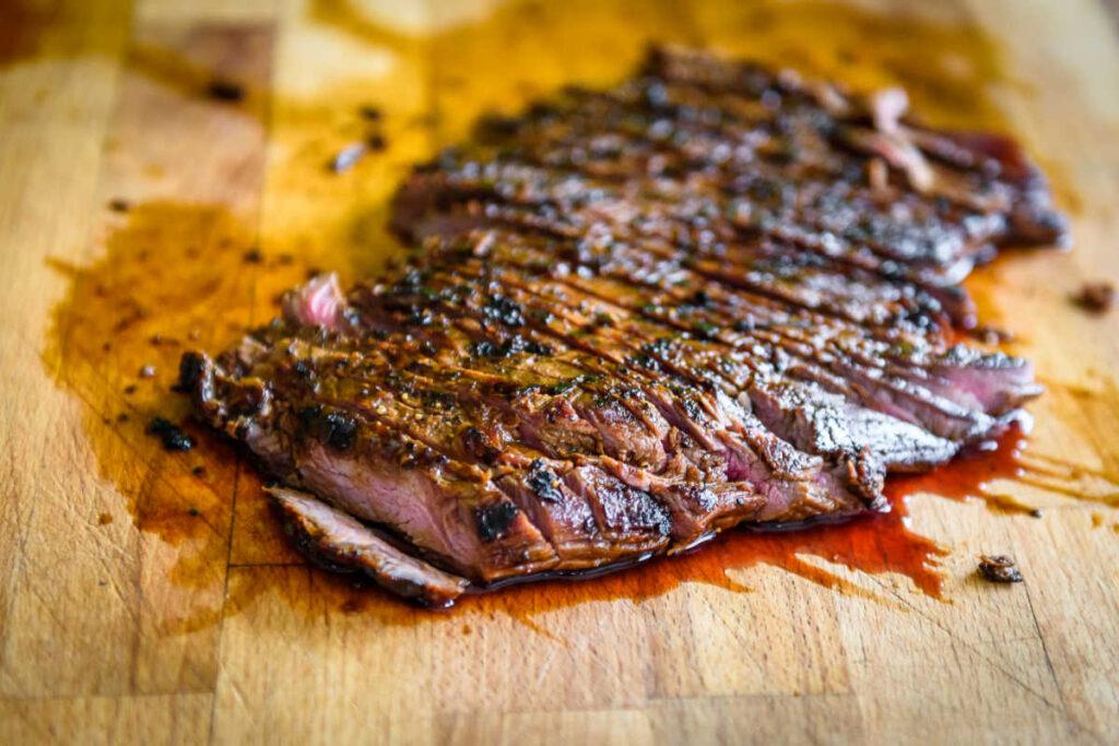 Grilled citrus marinated flank steak, sliced, on a wooden cutting board.