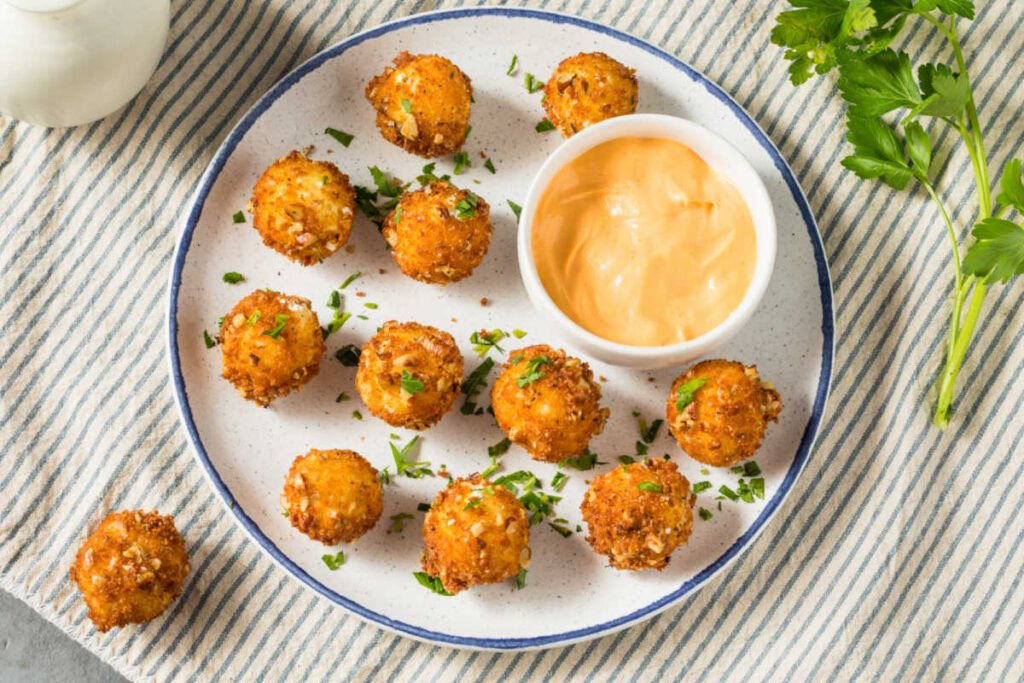 Overhead shot of a white plate with Fried Goat Cheese Balls with a mango dipping sauce in a small bowl on the side. The cheeseballs are garnished with grated Parmesan cheese and minced fresh parsley.