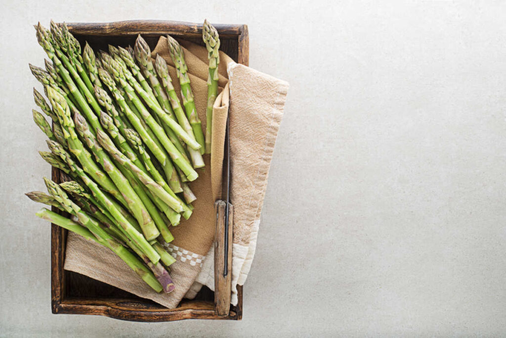 Top view of a bunch of raw, trimmed asparagus on a parchment lined baking pan.