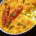 close-up of Cheddar Cheese Grits Casserole with bacon slices in baking dish