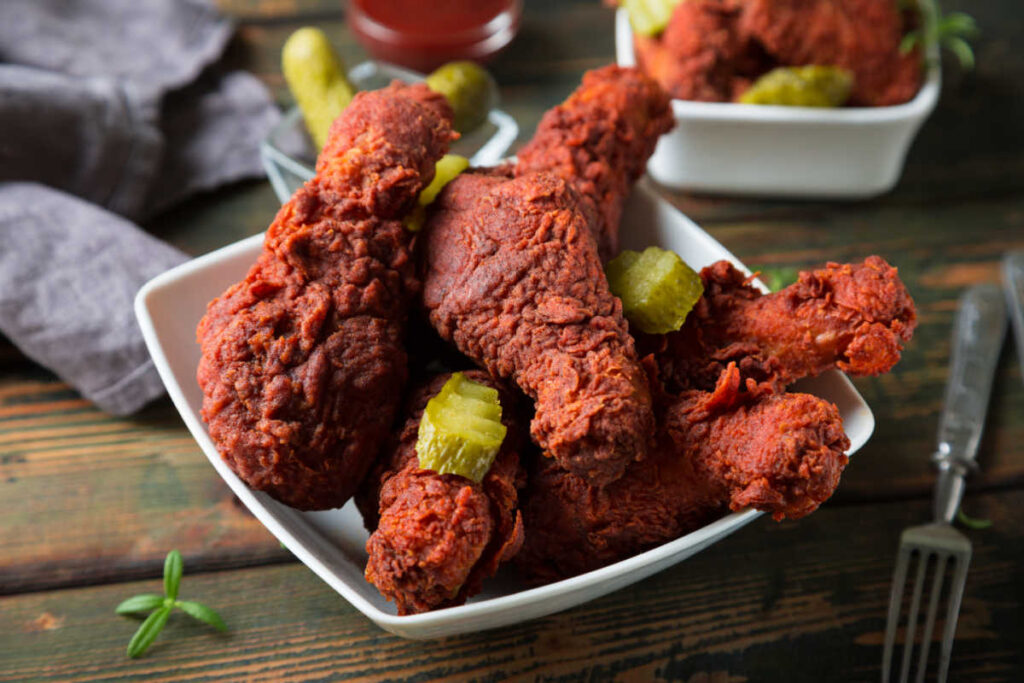 Top view of a white bowl of Flamin' Hot Nashville Chicken Wings and garnished with pickle slices.