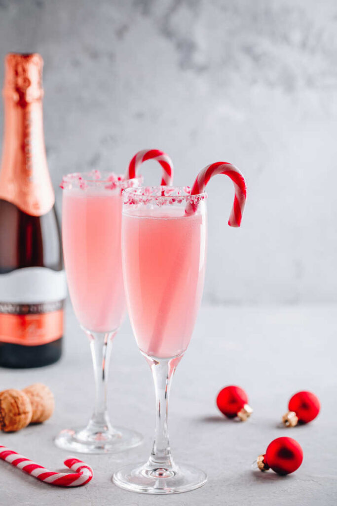 Sideview of a festive Christmas drink, this Santa's Peppermint Mimosa cocktail with prosecco and candy cane on gray stone concrete background.