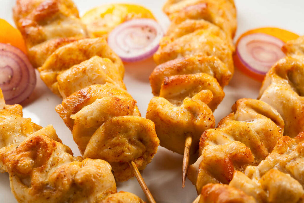 Skewers of Chicken Spiedini on a white plate and garnished with parsley, onion slices, and lemon wedges. Close up view.