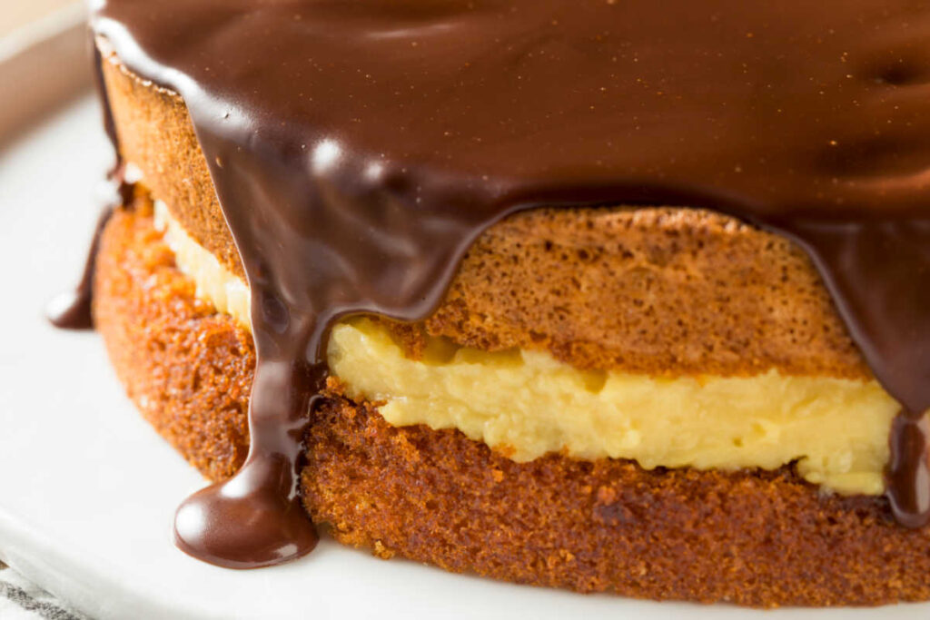 Close up view of a Boston Cream Pie on a white plate sitting upon a grey stripe towel.