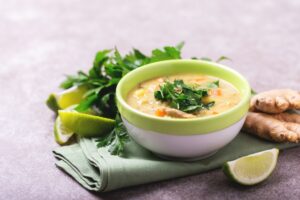 Green bowl of Indian Mulligawtawny Soup garnished with chopped parsley with lime wedges on the side. Side view.