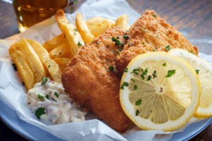 Plate with Beer Battered Fish, fries, a lemon wheel, and homemade tartar sauce on the side.