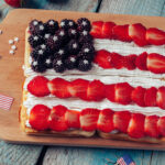 Wooden board with Patriotic Waffles. 4 homemade waffles with fresh blueberries, sliced strawberries , and whipped cream to make a flag. Perfect for the 4th of July.