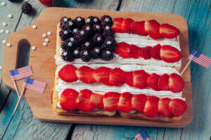 Wooden board with Patriotic Waffles. 4 homemade waffles with fresh blueberries, sliced strawberries , and whipped cream to make a flag. Perfect for the 4th of July.